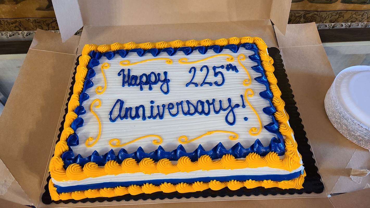 A quarter sheet cake with Happy 225th Anniversary written in frosting.