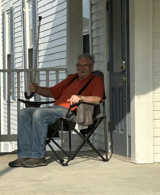 WB Bob Witham sitting on the porch with upraised cane.
